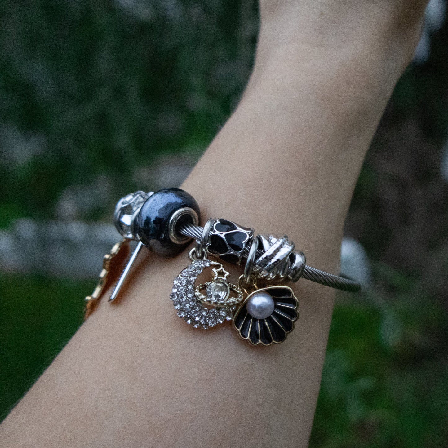 Close-up of a wrist wearing a bracelet with various charms against a blurred natural background