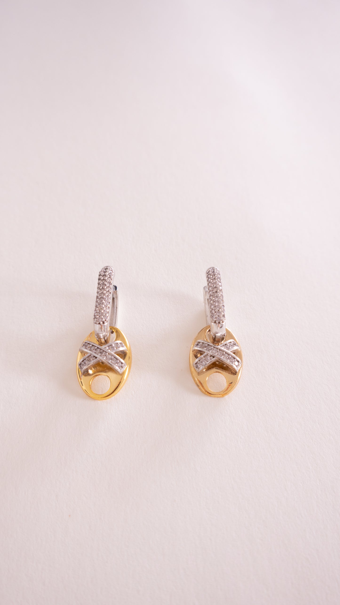 Pair of gold earrings with diamond accents on a light pink background