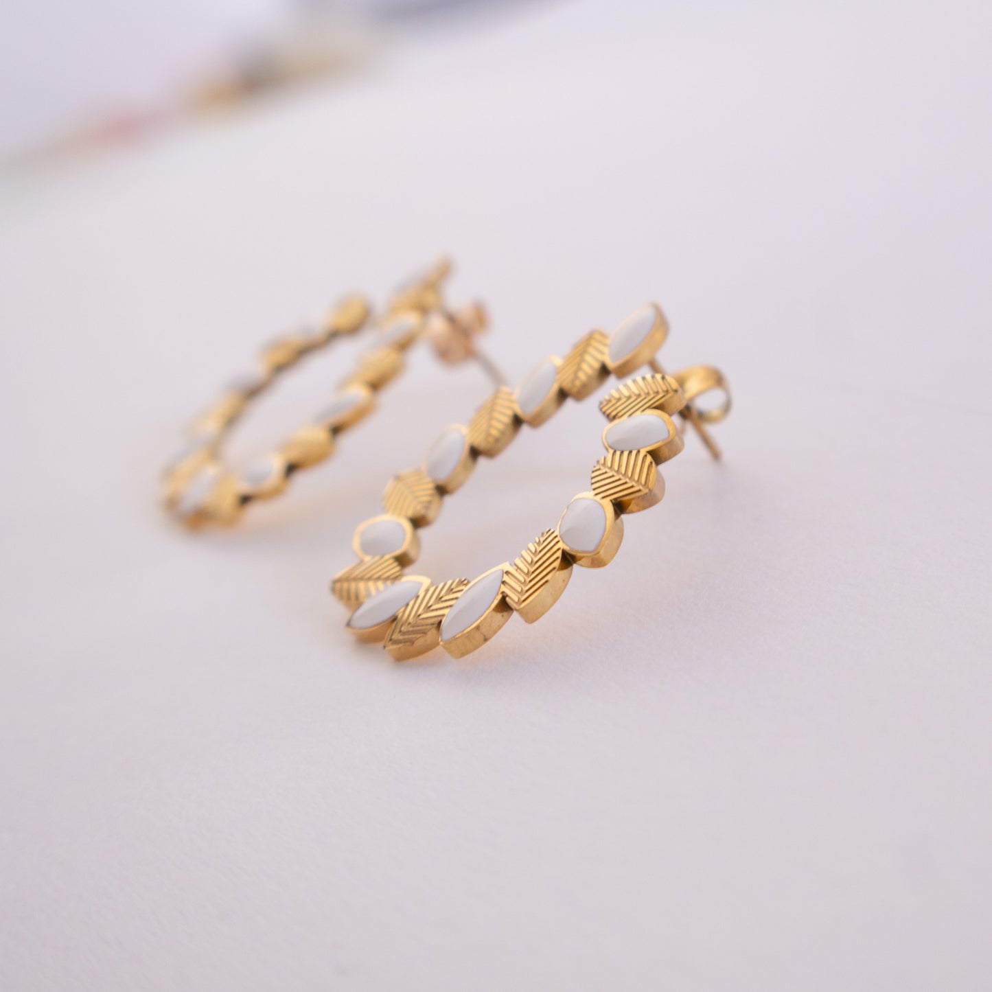 Gold hoop earrings with white accents on a light gray background