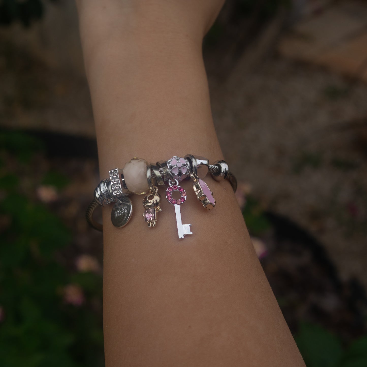 Hand wearing a bracelet with charms against a blurred natural background