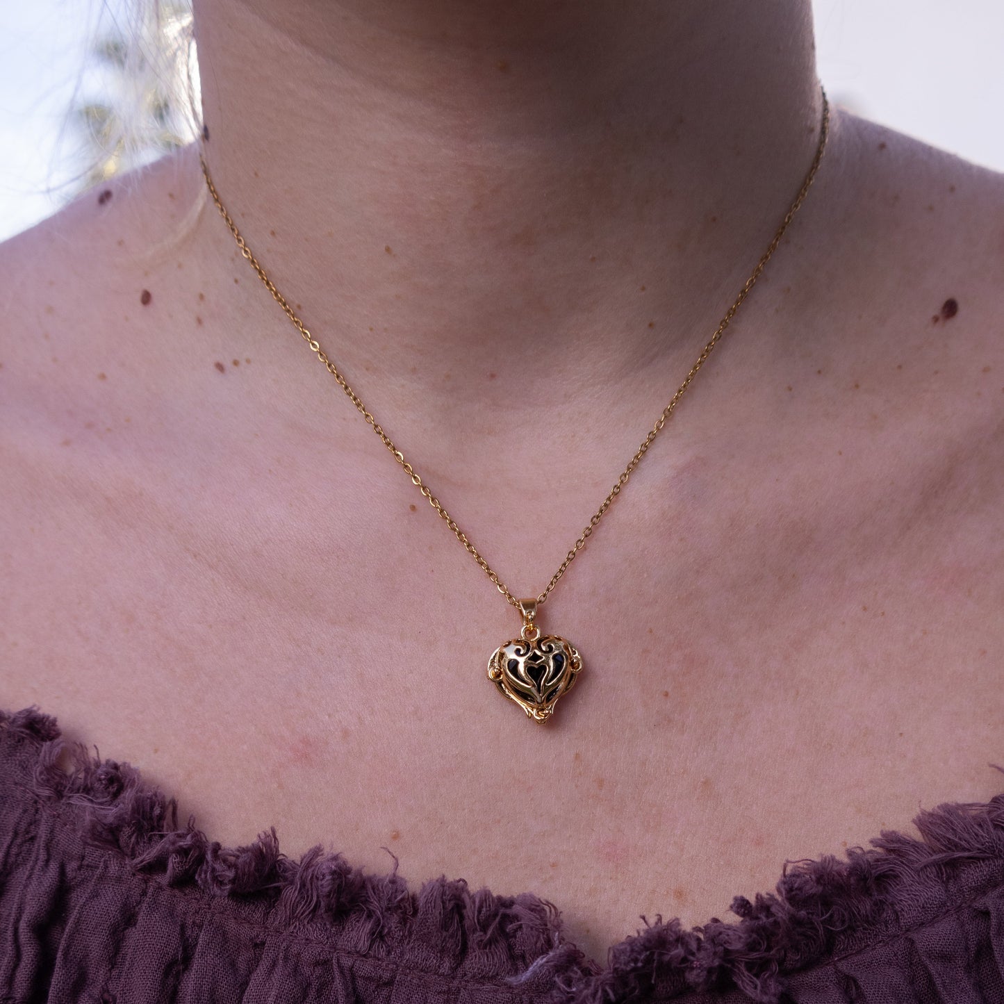 Necklace with a heart-shaped pendant worn by a person in a purple garment.