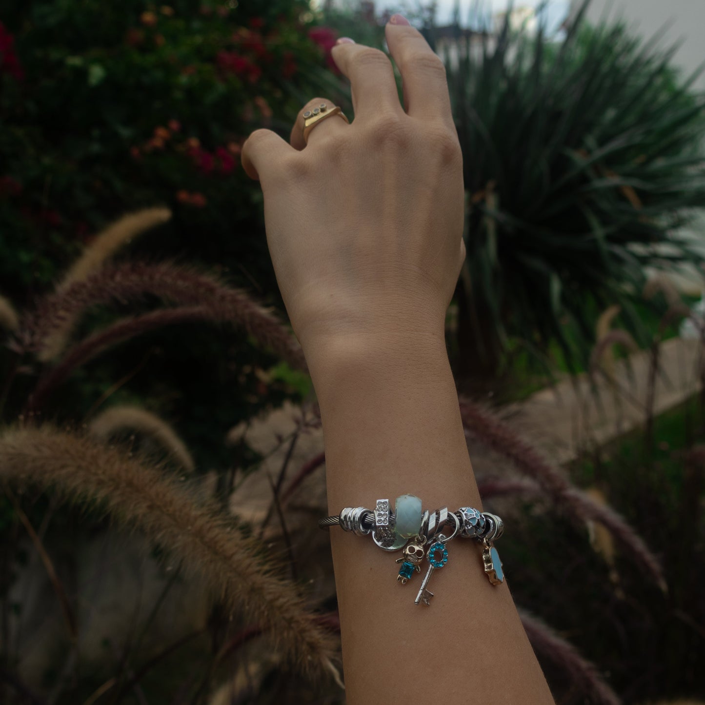 Hand with a bracelet reaching towards plants outdoors