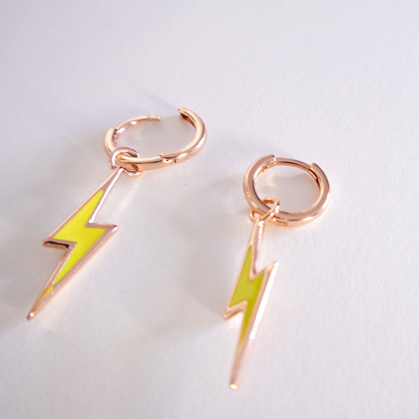 Pair of earrings with rose gold loops and green lightning bolt charms on a light gray background