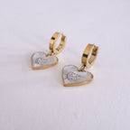 Heart-shaped earrings with gold and white details on a light gray background