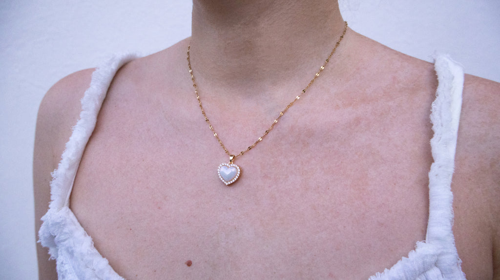Necklace with a heart-shaped pendant worn by a person in a white sleeveless top.