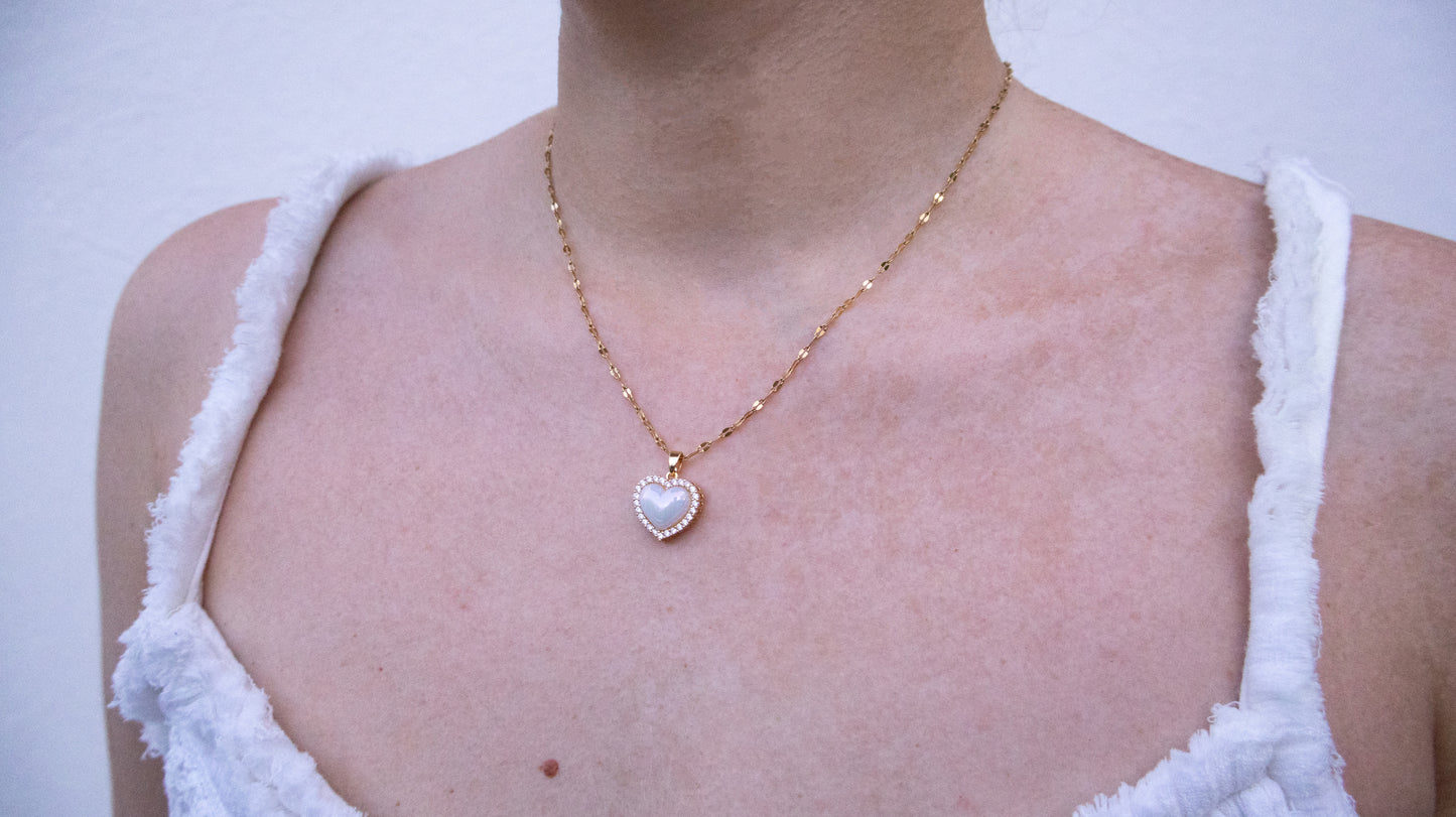 Necklace with a heart-shaped pendant worn by a person in a white sleeveless top.