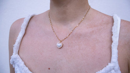 Necklace with a heart-shaped pendant worn by a person in a white sleeveless top.