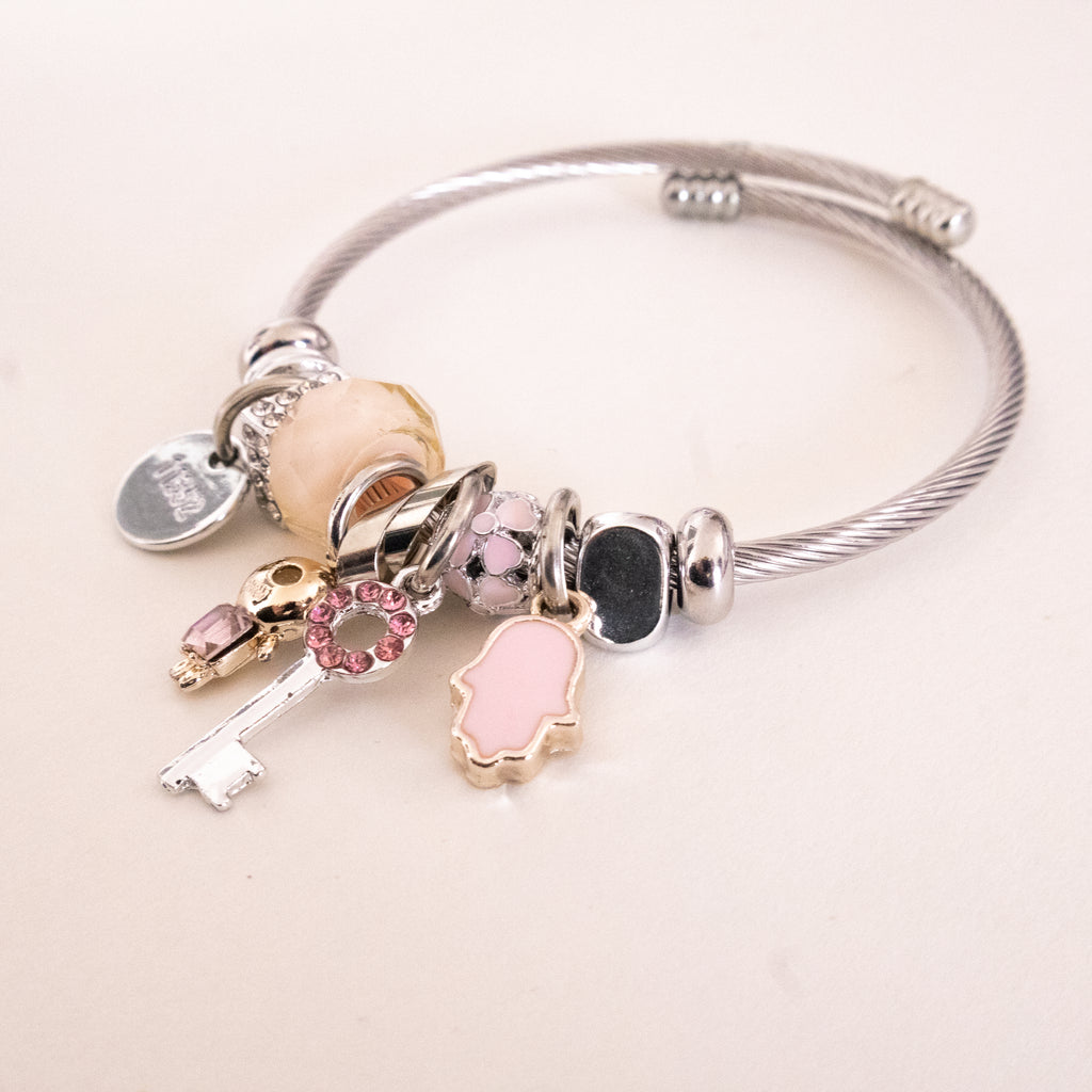 Silver bracelet with various charms on a light pink background