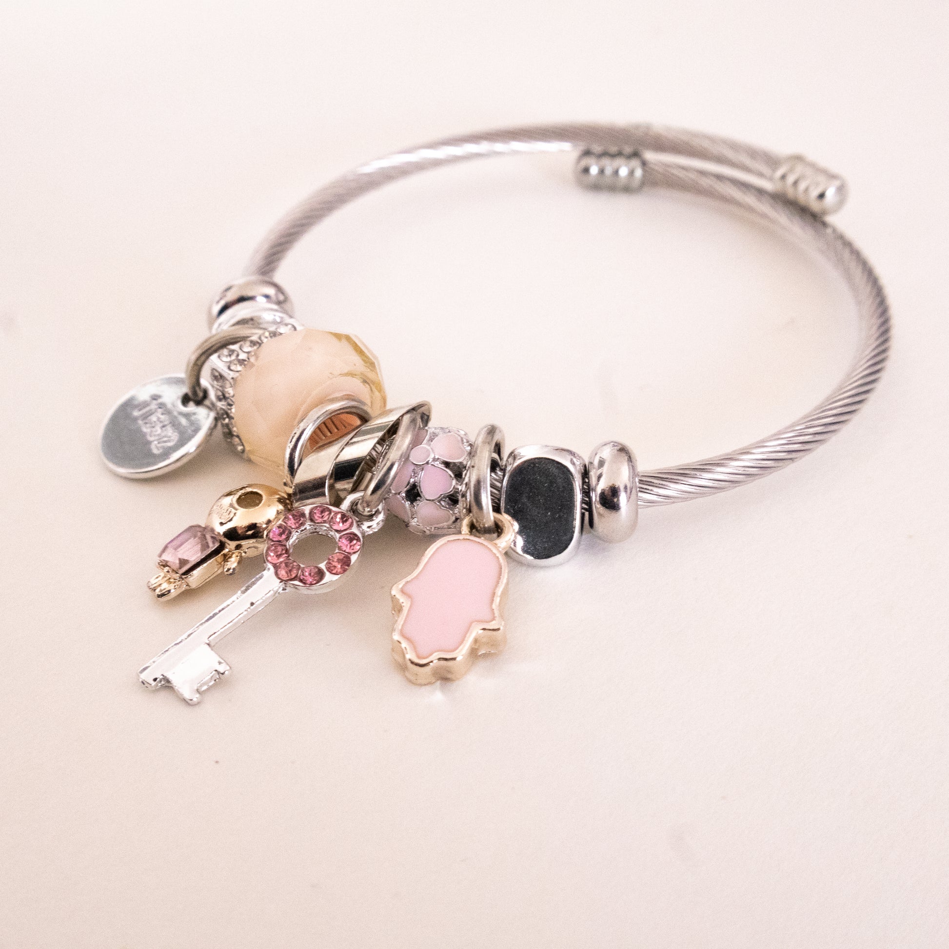 Silver bracelet with various charms on a light pink background