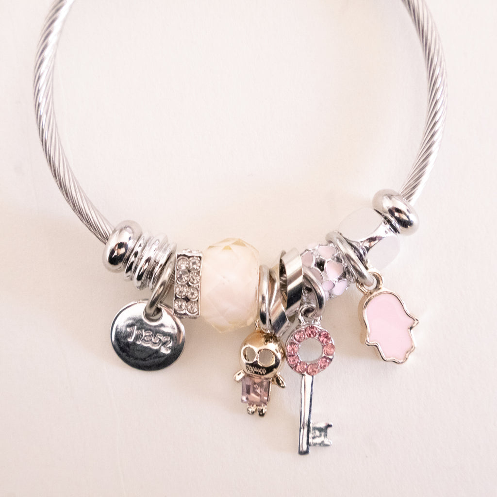 Silver bracelet with various charms on a light pink background