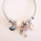 Silver bracelet with various charms on a light pink background