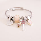 Silver bracelet with various charms on a light pink background