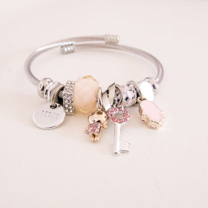 Silver bracelet with various charms on a light pink background