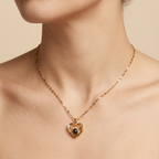 Gold heart-shaped necklace with a black gemstone on a beige background