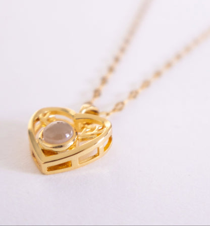 Gold heart-shaped necklace with a central gemstone on a white background