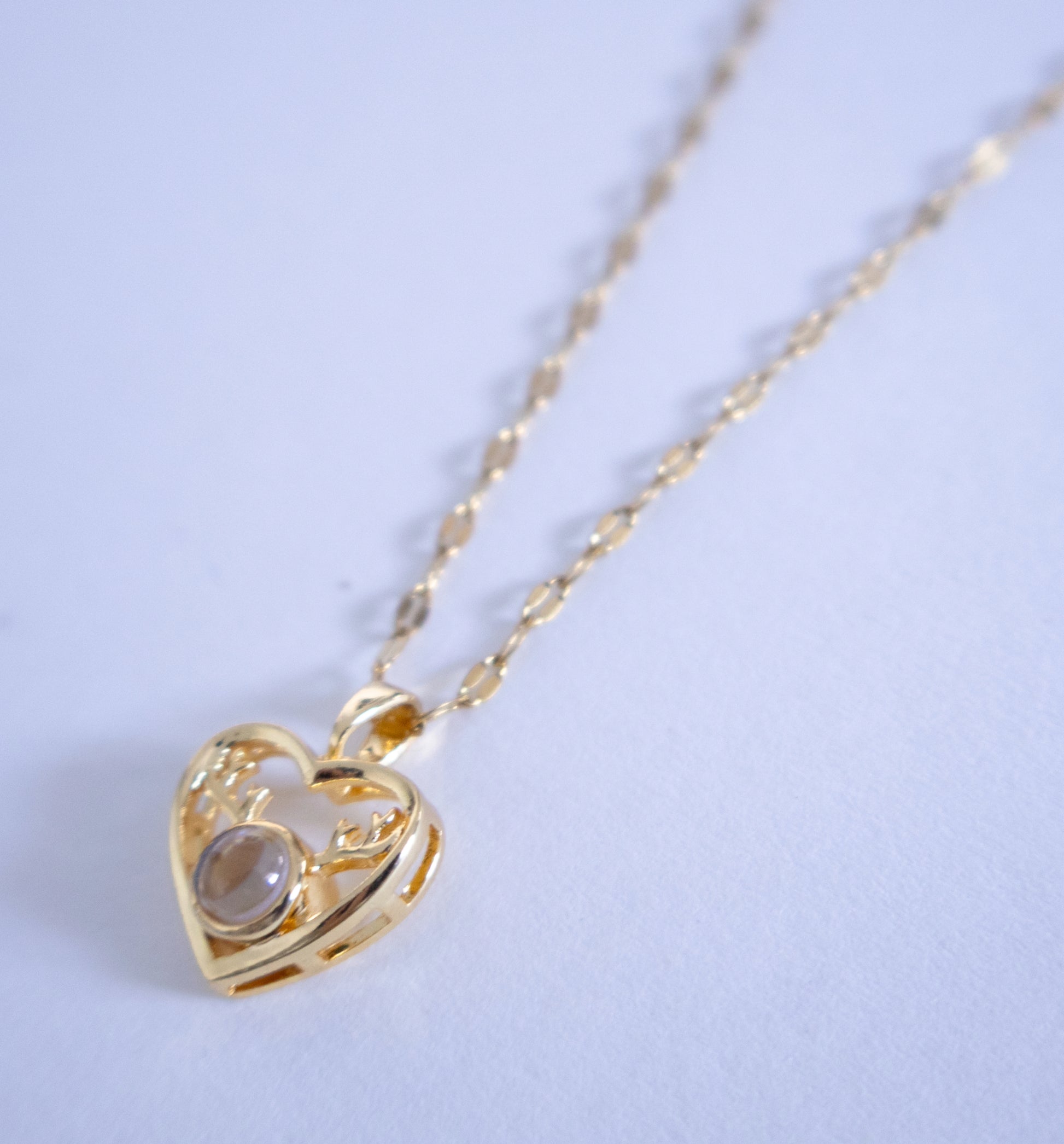 Gold heart-shaped necklace with a pendant on a light blue background