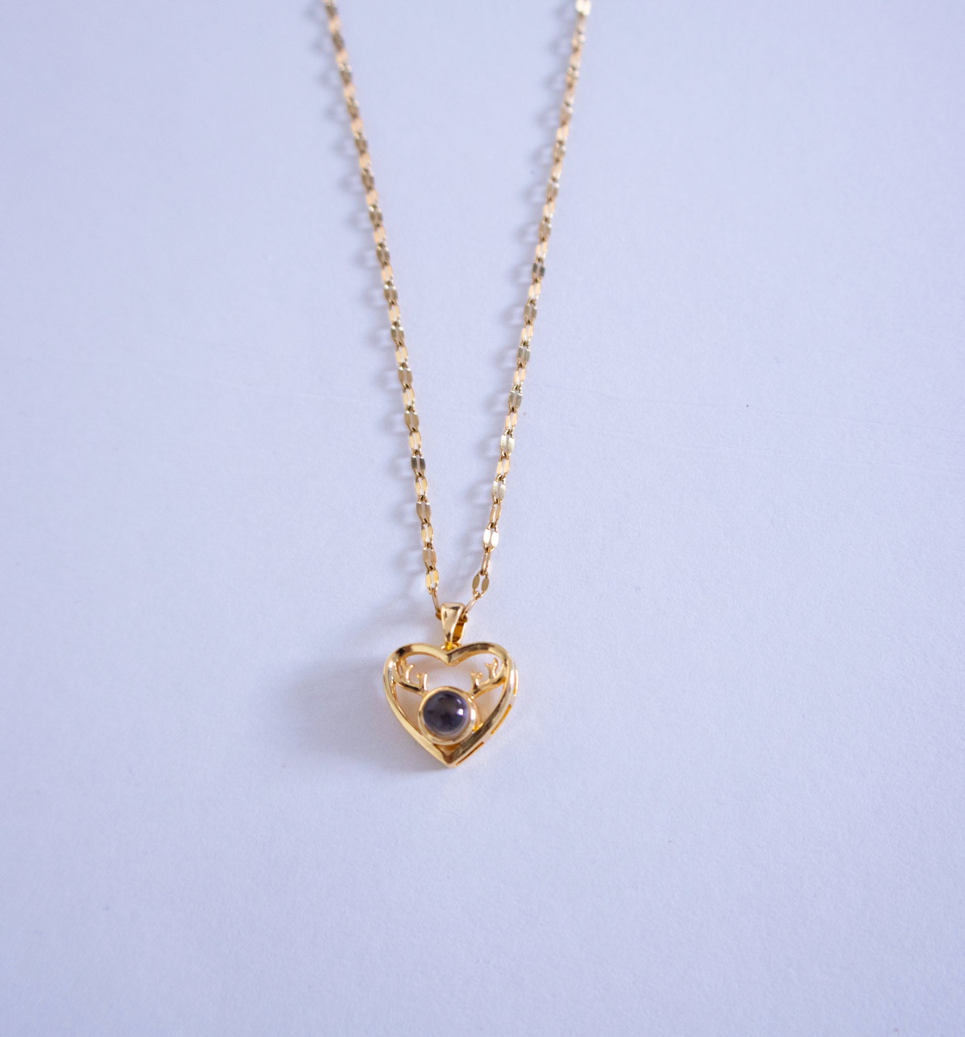 Gold heart-shaped necklace with a dark gemstone on a light purple background