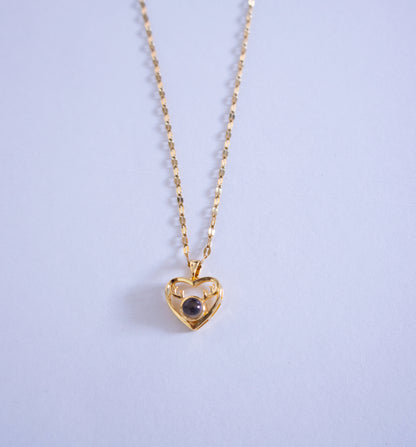 Gold heart-shaped necklace with a dark gemstone on a light purple background