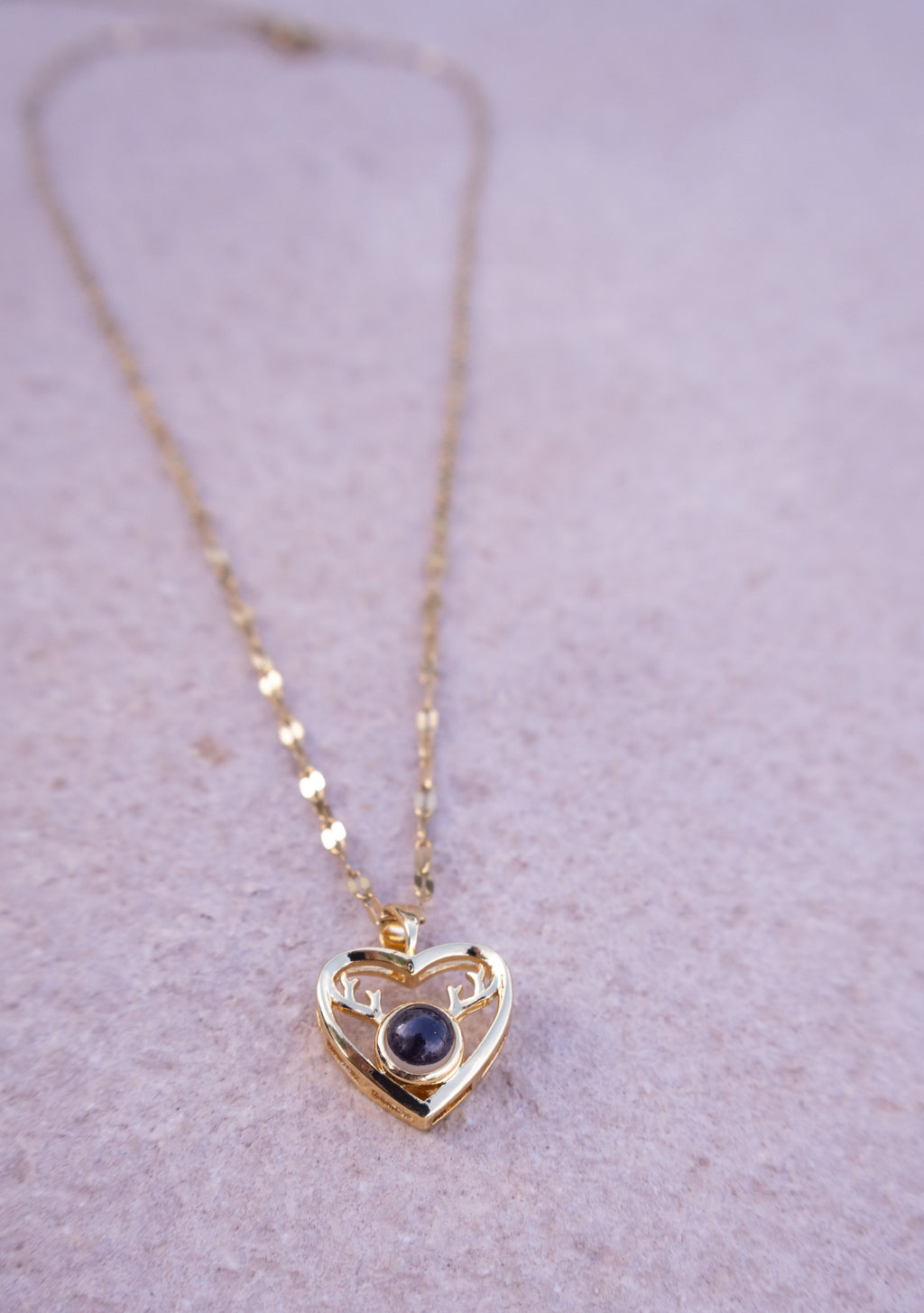 Gold heart-shaped necklace with a dark gemstone on a light purple background
