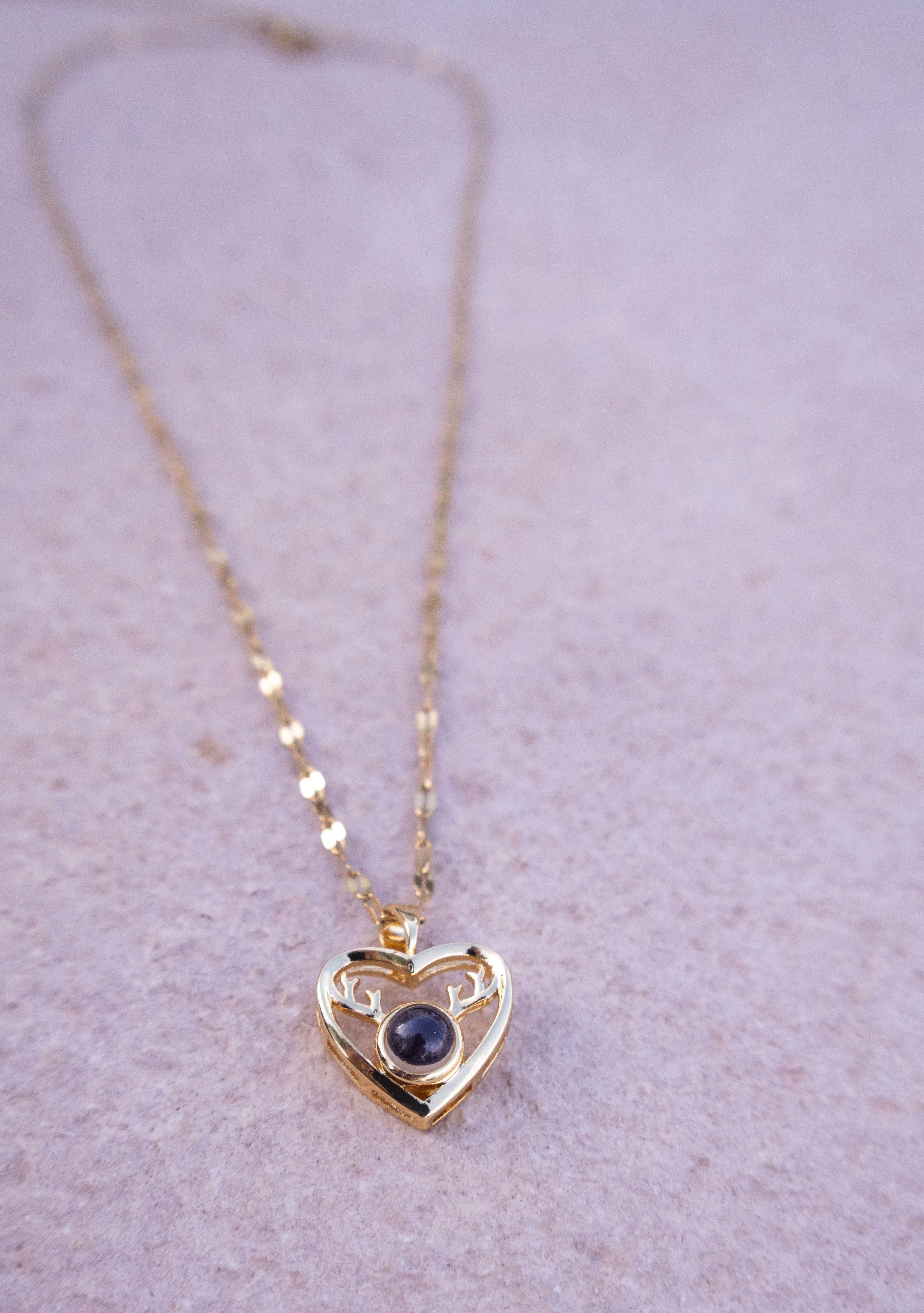 Gold heart-shaped necklace with a dark gemstone on a light purple background