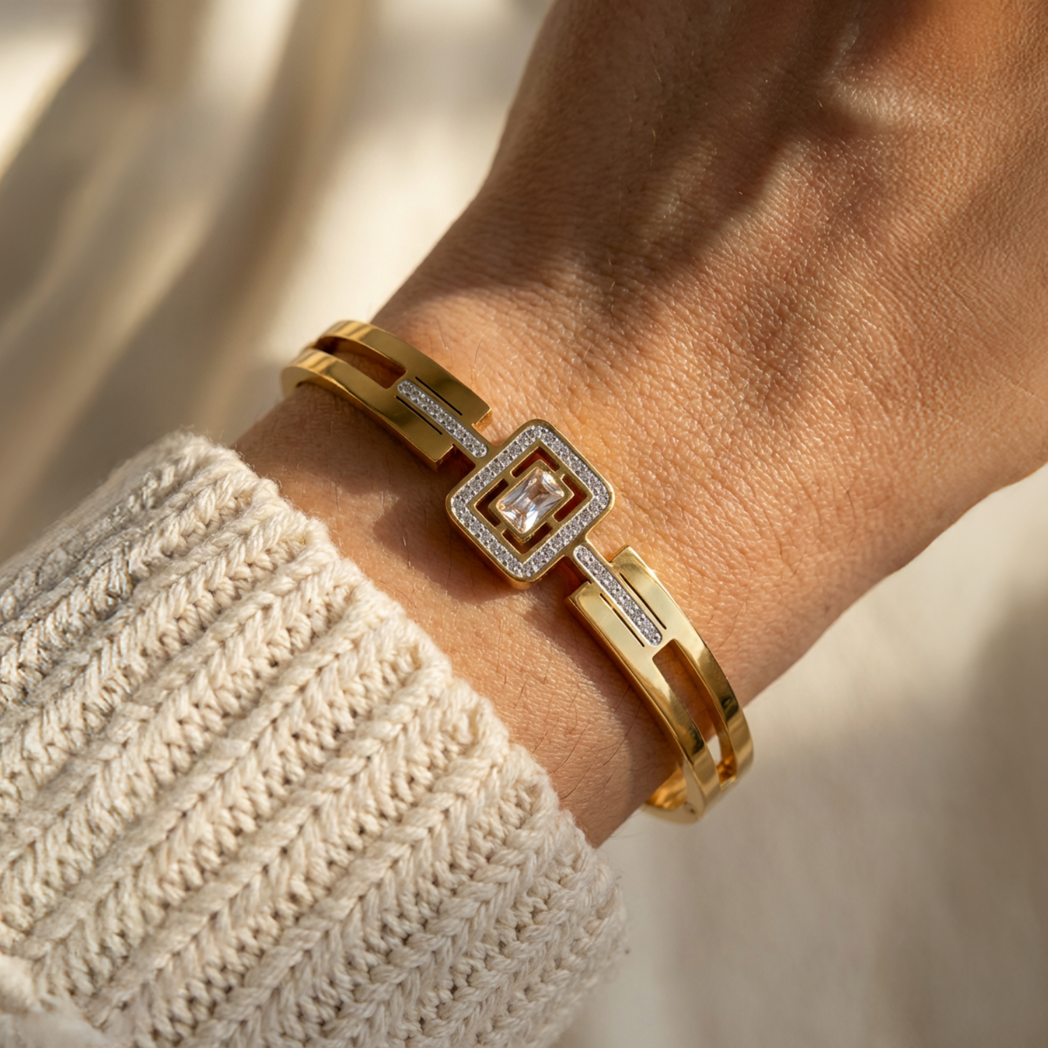 Gold bracelet with a square design worn on a wrist, with a blurred background.