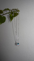Necklace with a blue pendant hanging against a plain wall