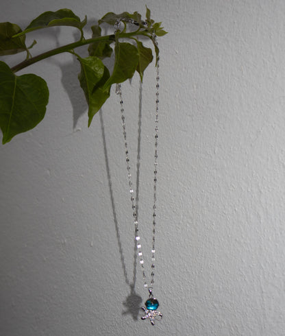 Necklace with a blue pendant hanging against a plain wall