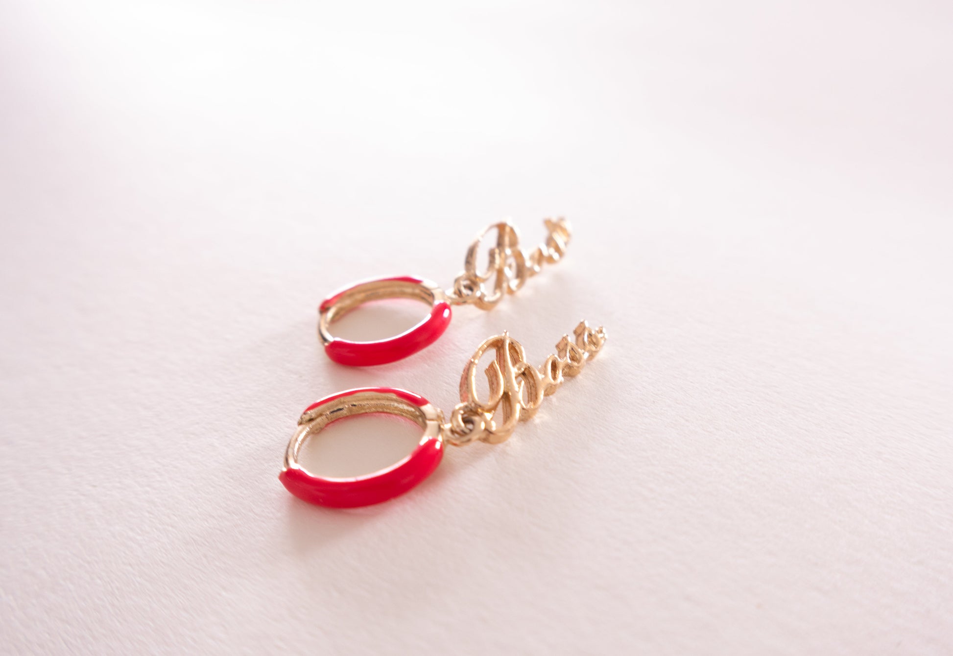 Gold and red earrings on a light pink background