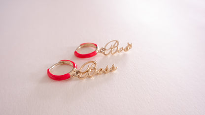 Gold hoop earrings with red accents on a light pink background