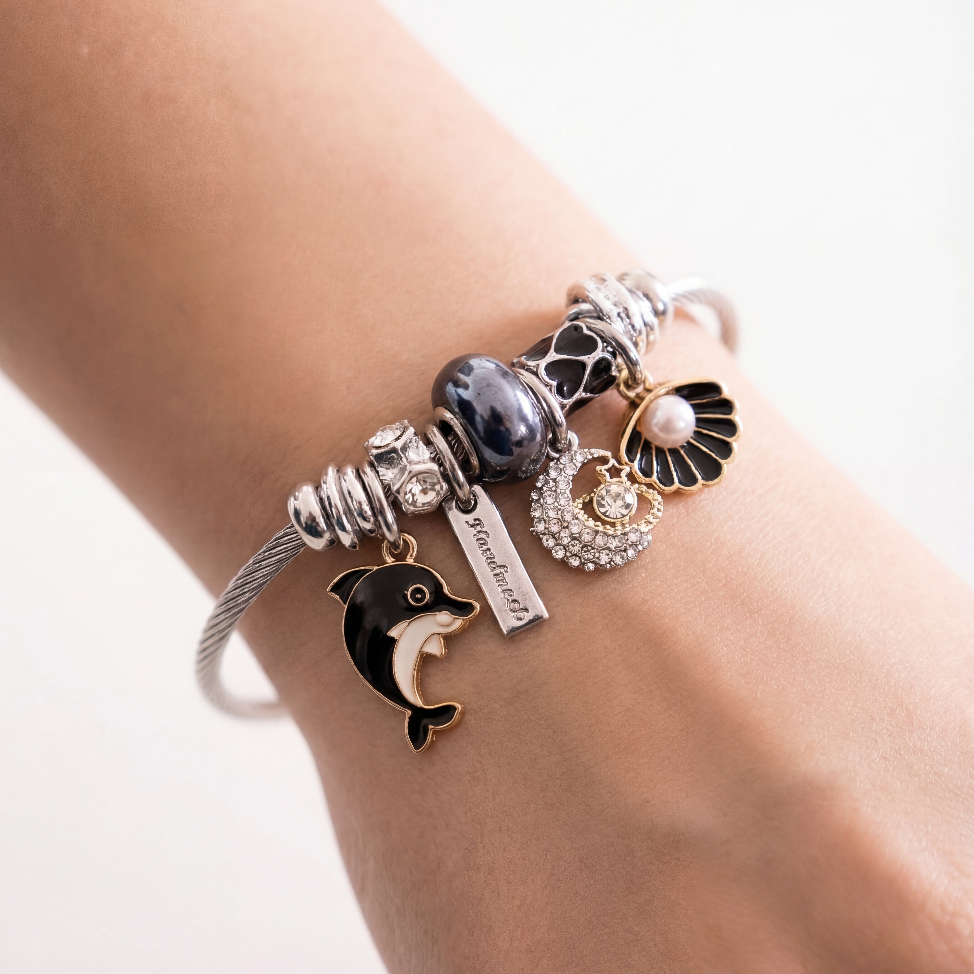 Bracelet with various charms including a dolphin on a wrist against a light background