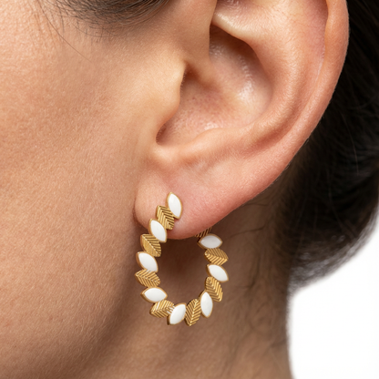 Close-up of an ear wearing gold and white hoop earrings on a neutral background
