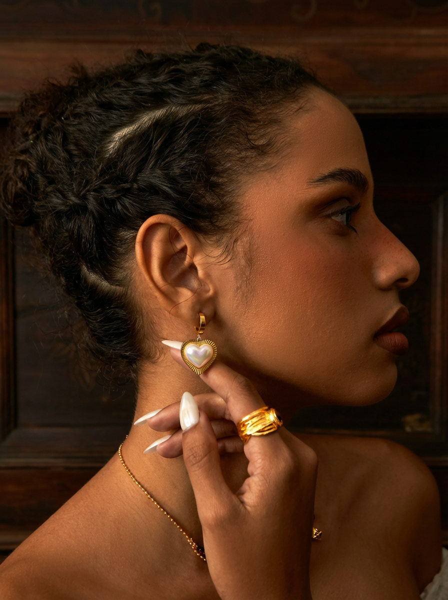 Woman wearing gold earrings and a ring, with a warm-toned background