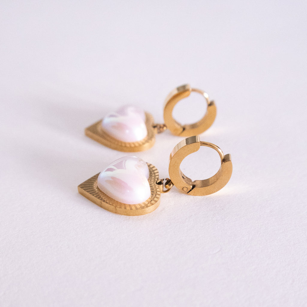 Gold hoop earrings with heart-shaped pearl-like stones on a light background