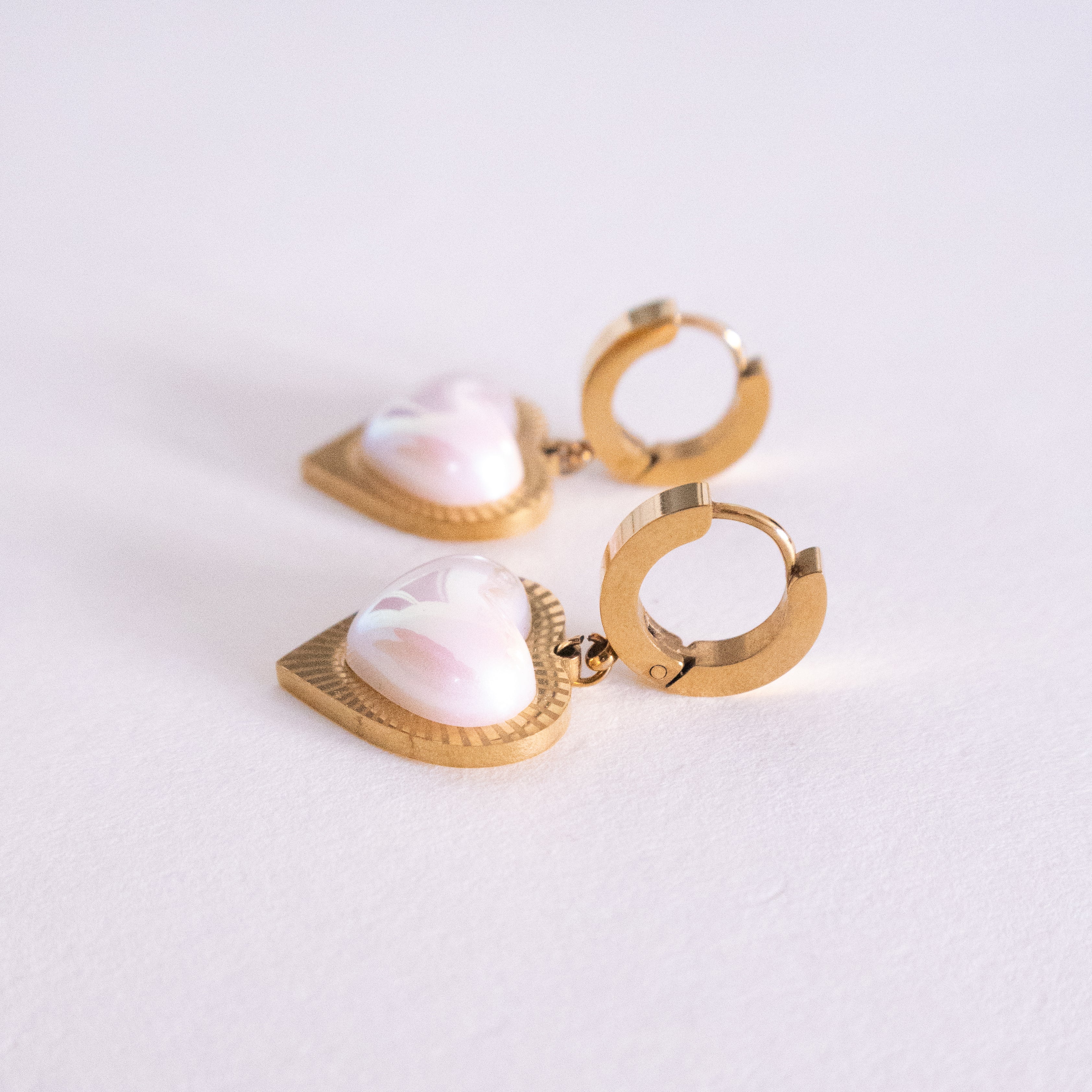 Gold hoop earrings with heart-shaped pearl-like stones on a light background