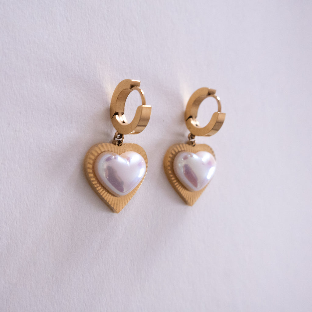 Gold heart-shaped earrings with pearl-like centers on a light gray background