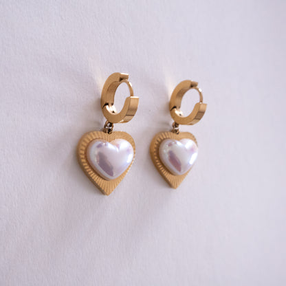Gold heart-shaped earrings with pearl-like centers on a light gray background