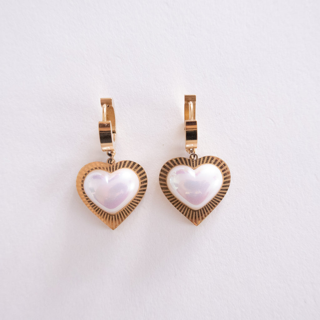 Heart-shaped earrings with gold frame and white center on a light gray background