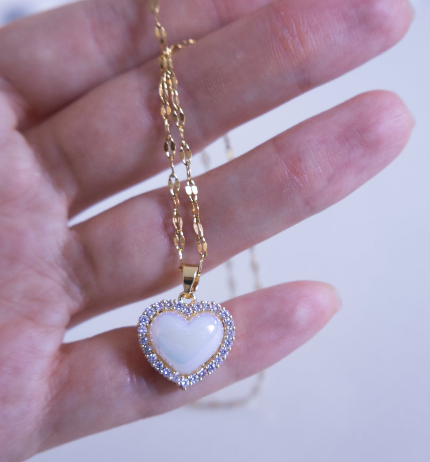 Gold necklace with a heart-shaped pendant held by a hand against a white background