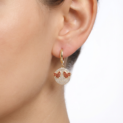 Gold earrings with red gemstones worn by a person on a white background
