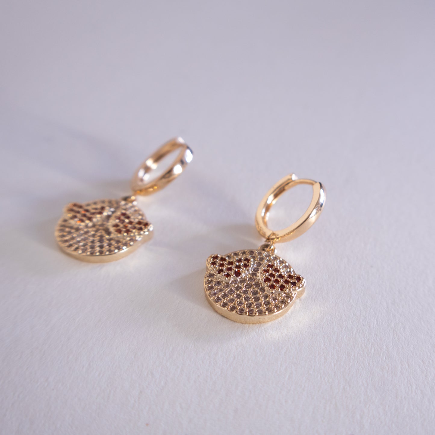 Gold earrings with circular designs on a light gray background