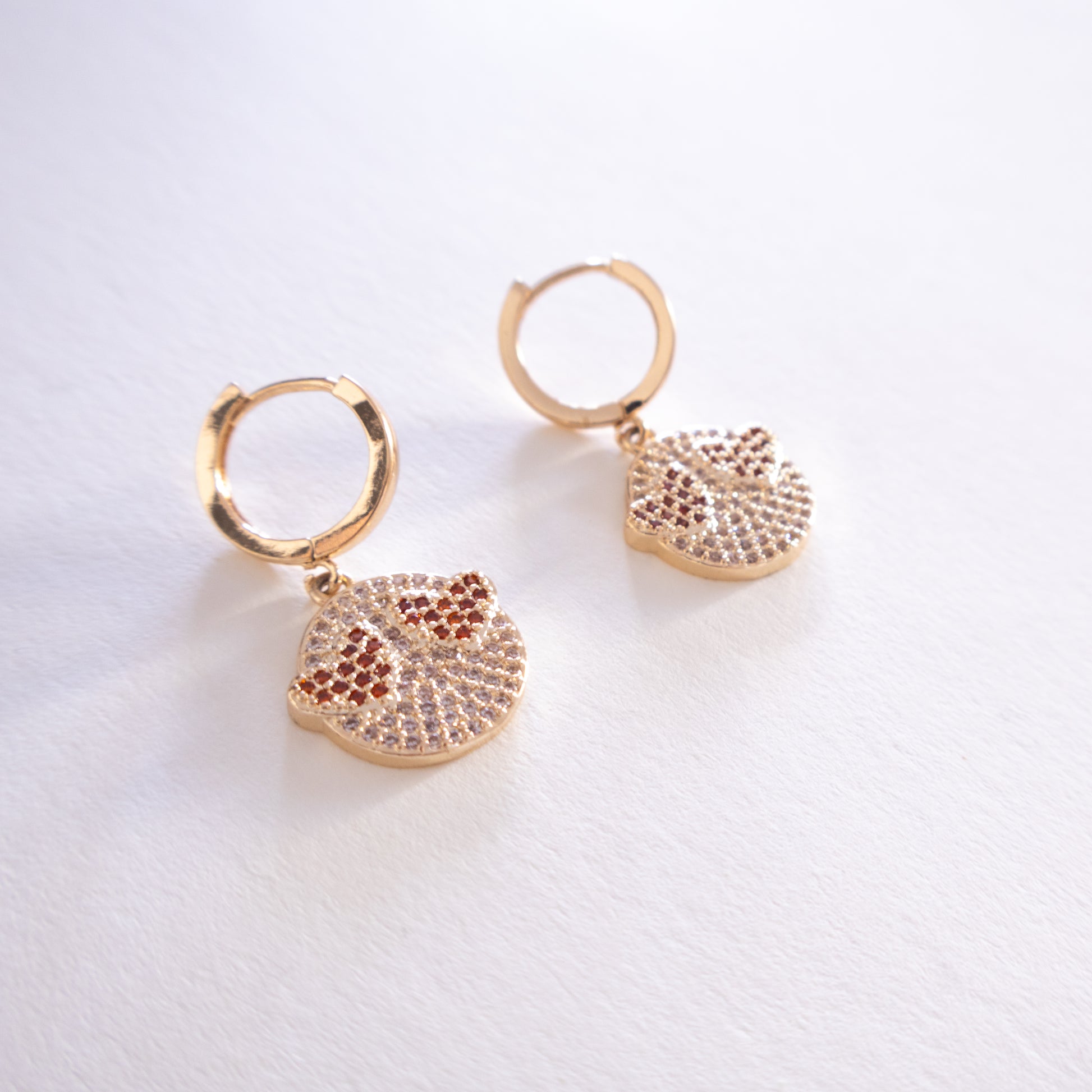 Gold hoop earrings with leaf-shaped pendants on a light background