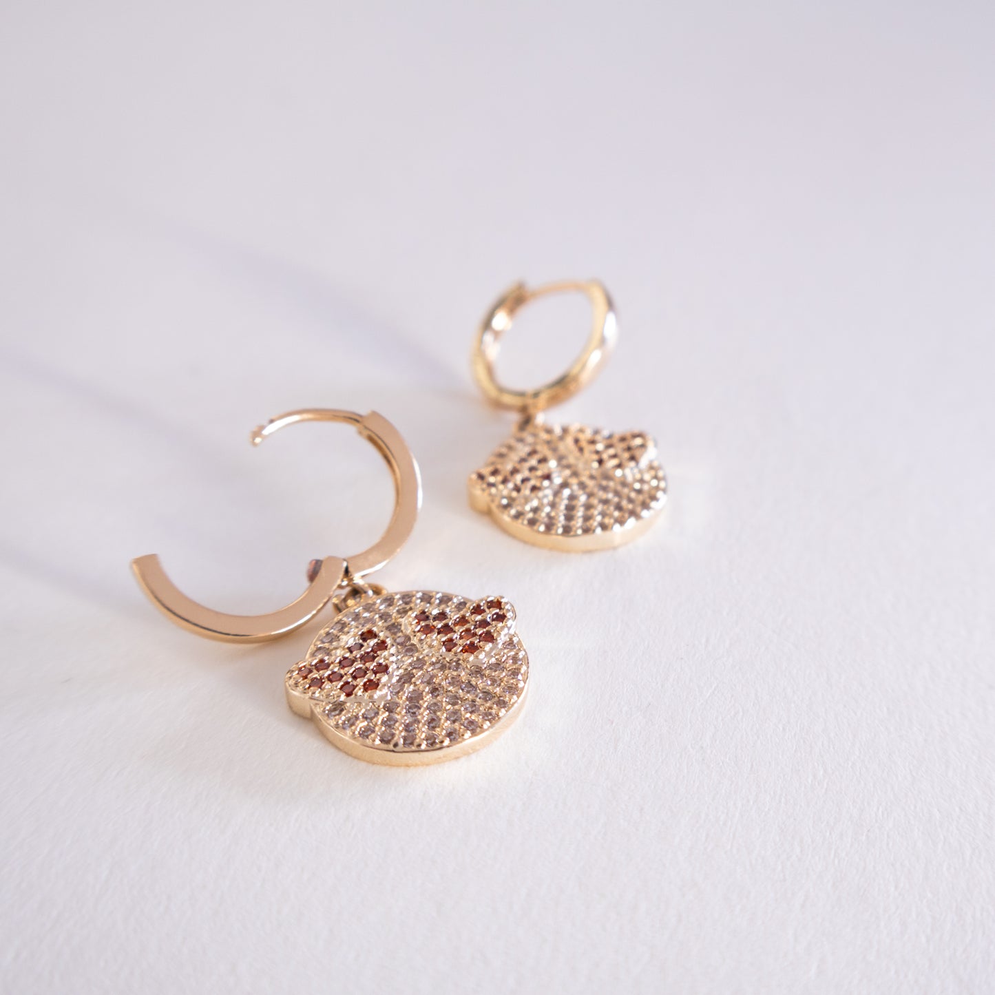 Pair of gold hoop earrings with round, diamond-studded pendants on a light gray background