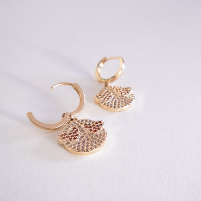 Pair of gold hoop earrings with round, diamond-studded pendants on a light gray background