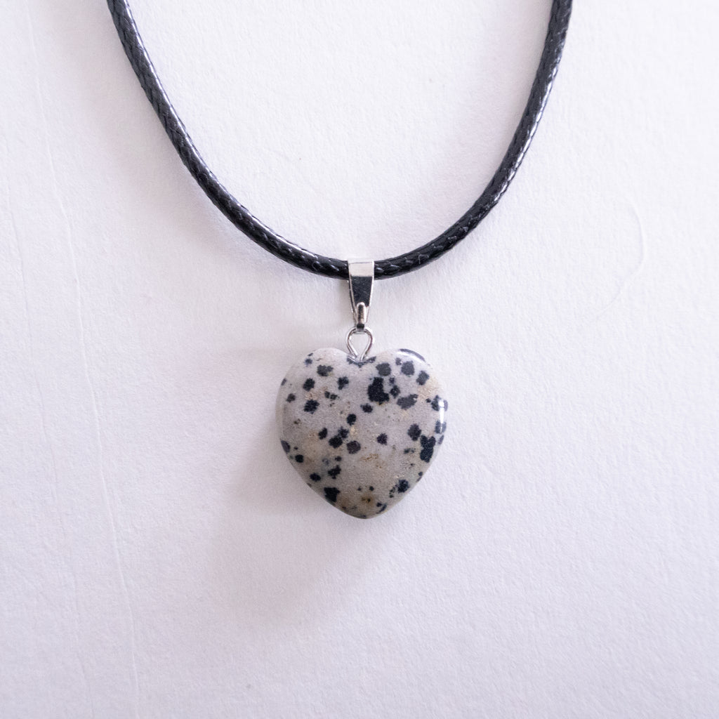 Heart-shaped dalmatian jasper pendant on a black cord against a white background