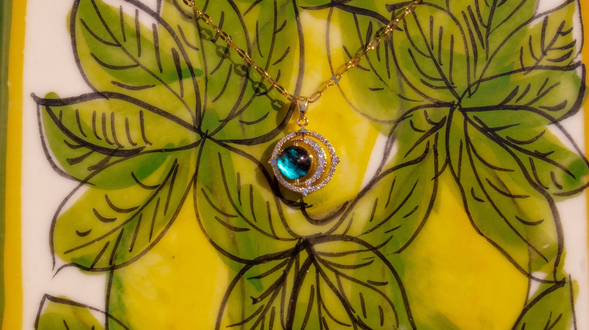 Decorative tile with green leaf design and a central blue gemstone on a white background