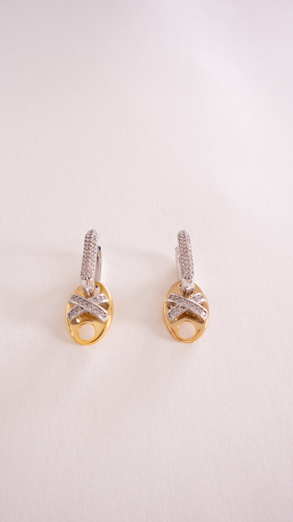 Pair of gold earrings with diamond accents on a light pink background