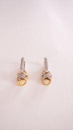 Pair of gold earrings with diamond accents on a light pink background