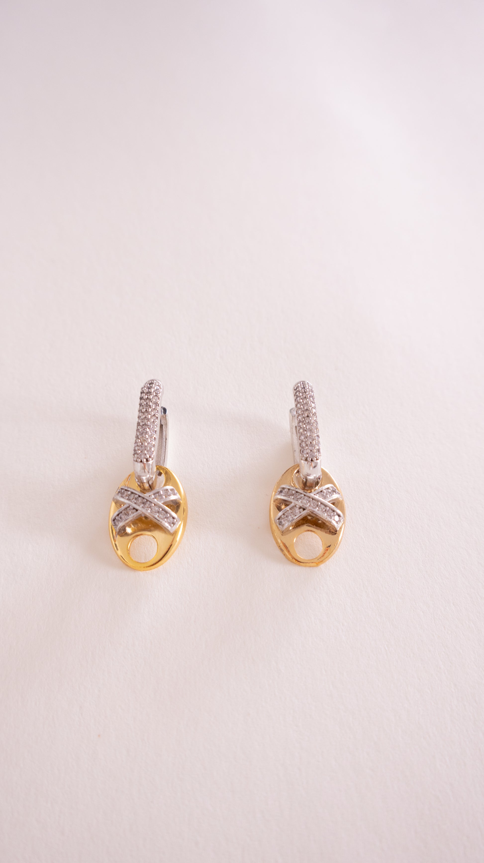 Pair of gold earrings with diamond accents on a light pink background