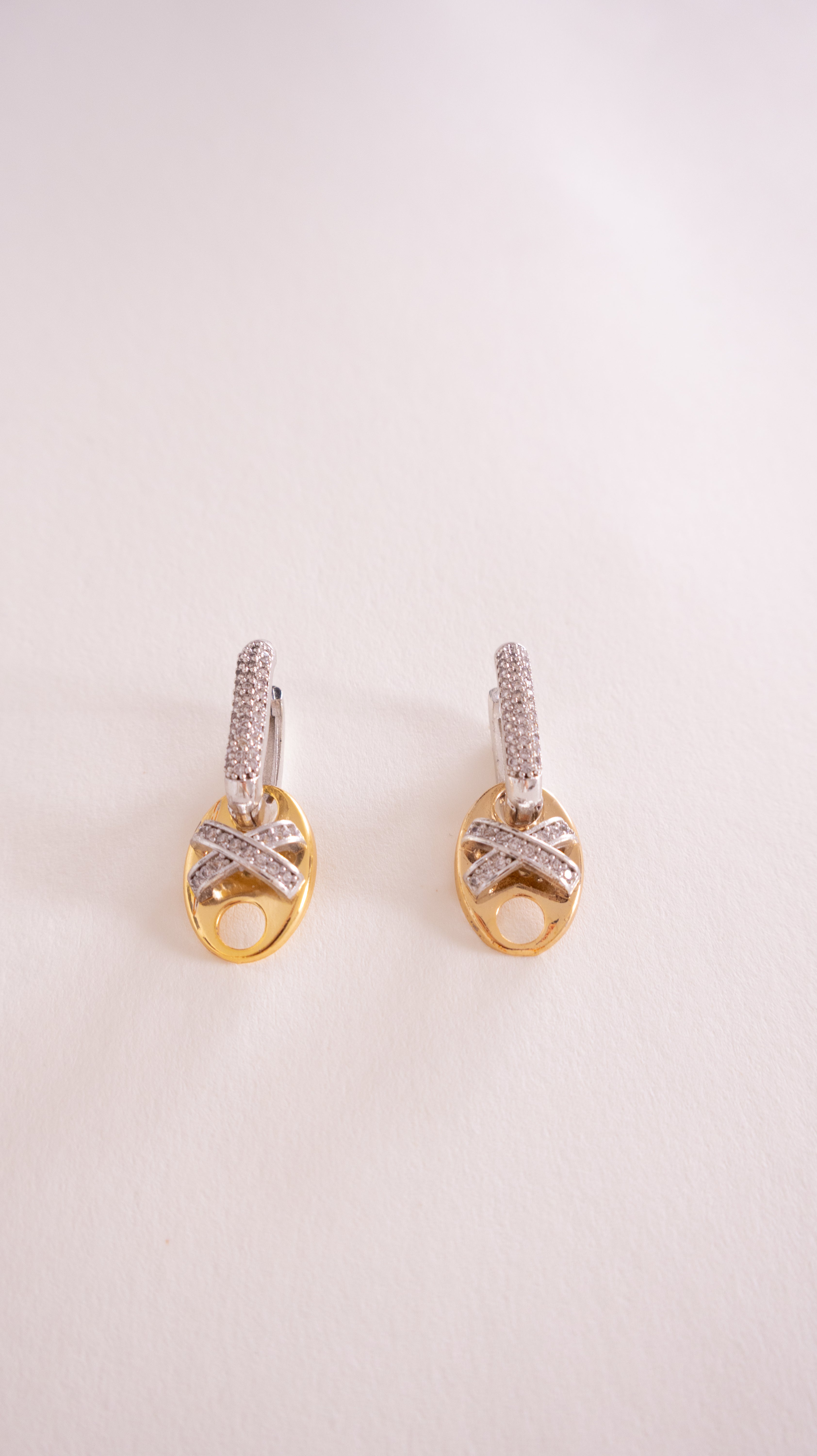 Pair of gold earrings with diamond accents on a light pink background