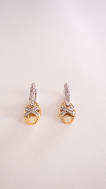 Pair of gold earrings with diamond accents on a light pink background